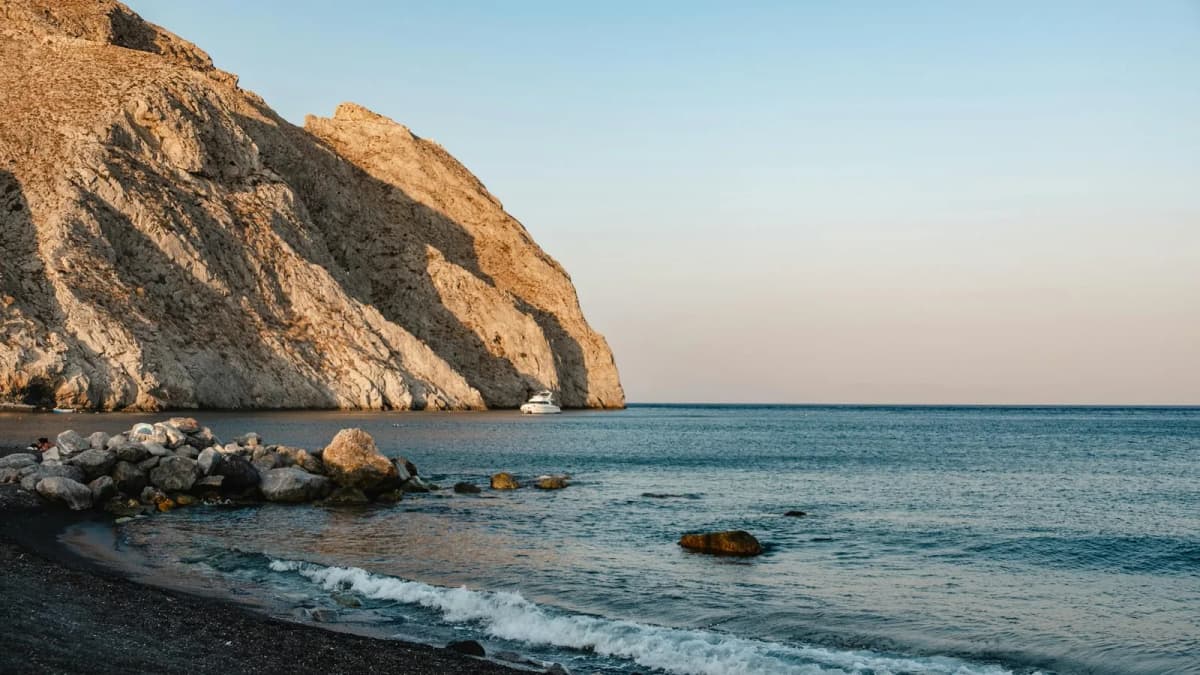 Dark sand beach below a steep rocky headland in Santorini