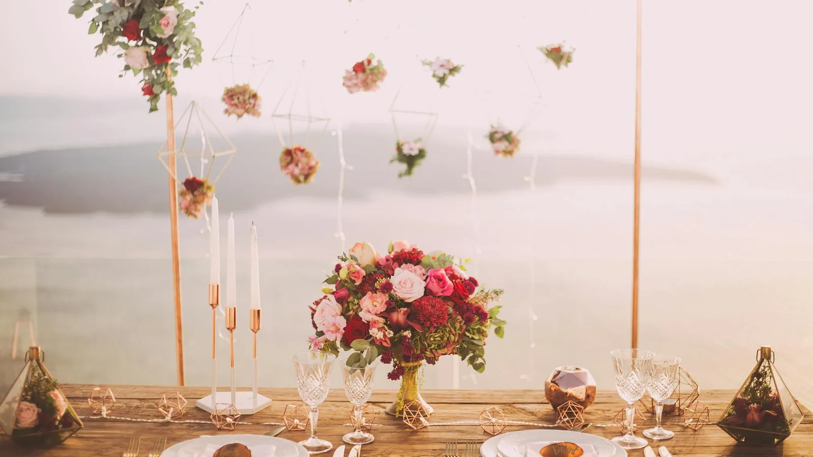 Romantic dinner setup overlooking the Santorini caldera at sunset with candles and flowers