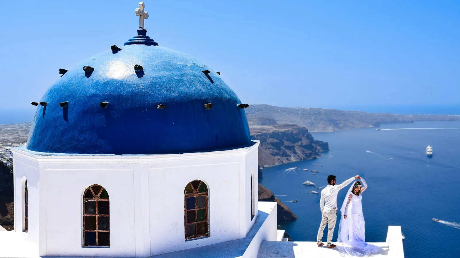 Couple celebrating their proposal by a blue dome church overlooking the Santorini caldera