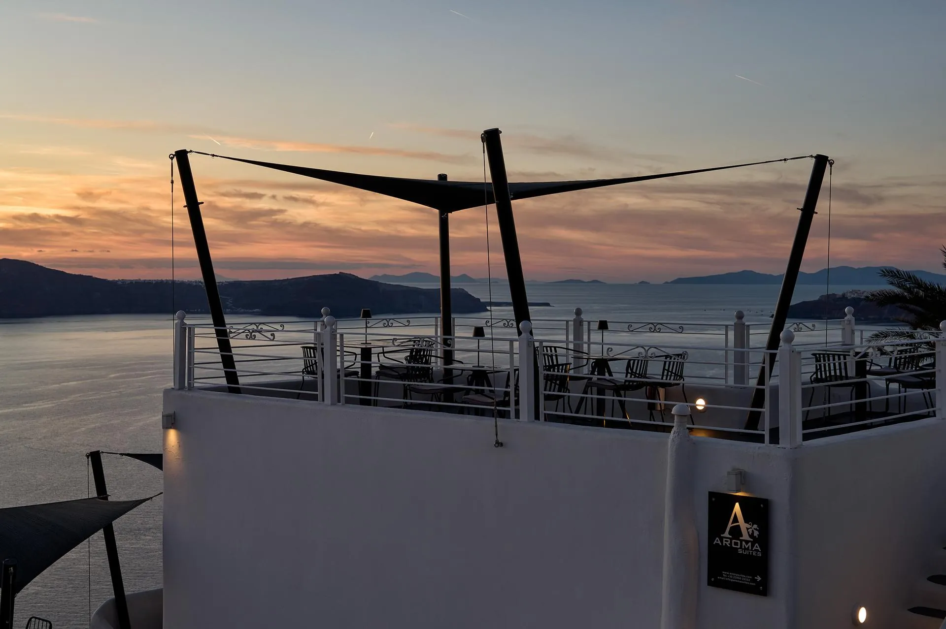 Rooftop terrace with sail shade at sunset with Aroma Suites sign visible